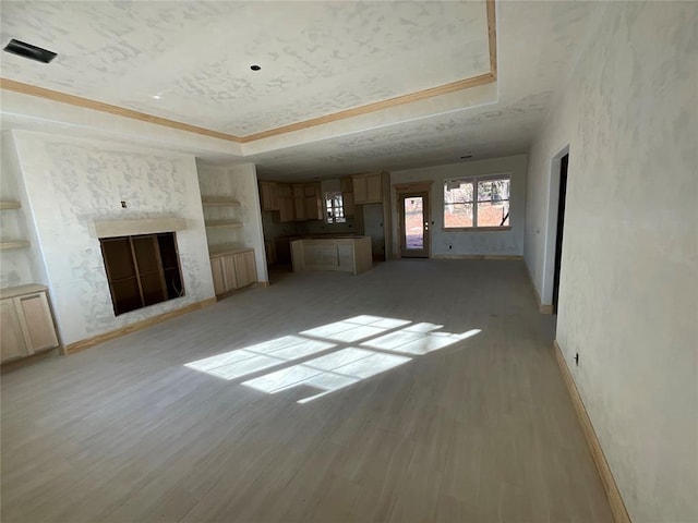 unfurnished living room with a tray ceiling, built in shelves, a fireplace, and light wood finished floors