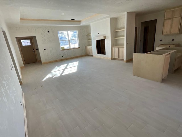 unfurnished living room featuring a fireplace, a raised ceiling, built in features, and a healthy amount of sunlight