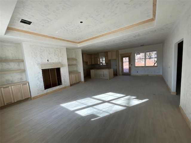 unfurnished living room featuring a raised ceiling, light wood-type flooring, and a high end fireplace