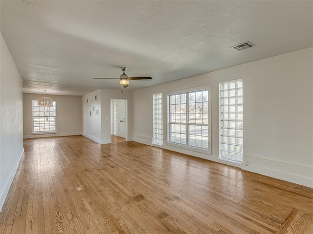 unfurnished living room featuring ceiling fan with notable chandelier, light wood-type flooring, and a textured ceiling