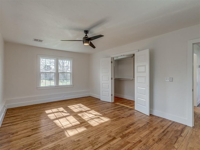 unfurnished bedroom featuring ceiling fan, a closet, a walk in closet, and light hardwood / wood-style flooring