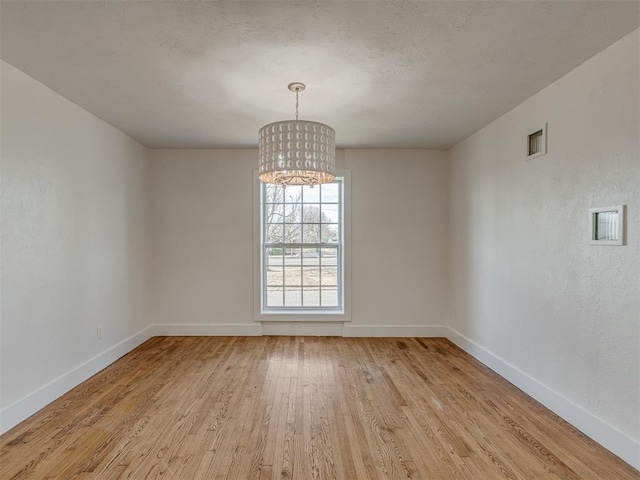 empty room with light hardwood / wood-style floors and a chandelier