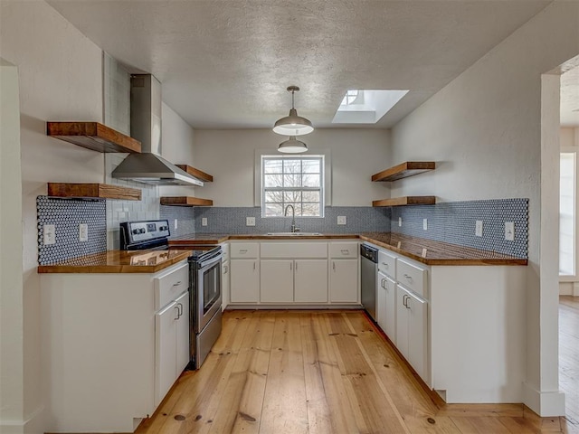 kitchen featuring sink, stainless steel appliances, wall chimney range hood, pendant lighting, and white cabinets