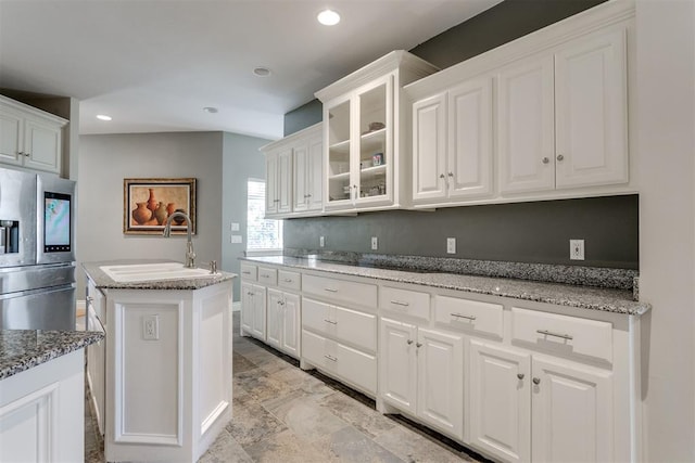 kitchen featuring sink, stainless steel fridge, a kitchen island, light stone counters, and white cabinetry