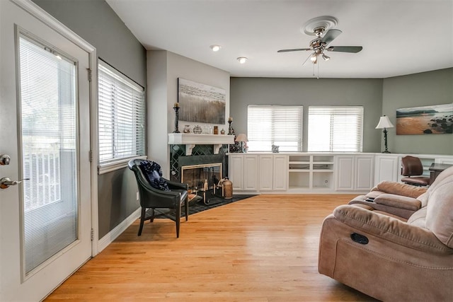 living room featuring a tiled fireplace, light hardwood / wood-style flooring, plenty of natural light, and ceiling fan