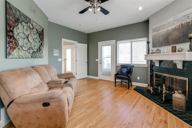 living room with ceiling fan, light hardwood / wood-style floors, and a tile fireplace