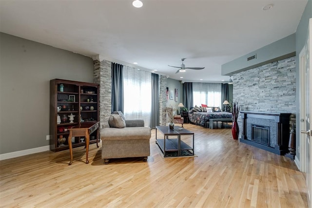 living room with a stone fireplace, ceiling fan, and light hardwood / wood-style floors