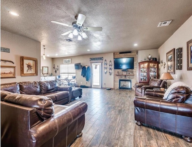 living room featuring a fireplace, ceiling fan, and a textured ceiling