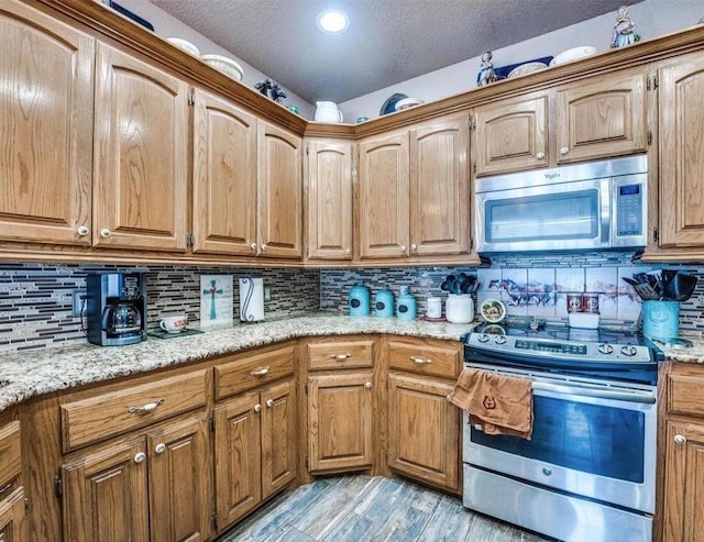 kitchen with light stone countertops, appliances with stainless steel finishes, light wood-type flooring, and tasteful backsplash