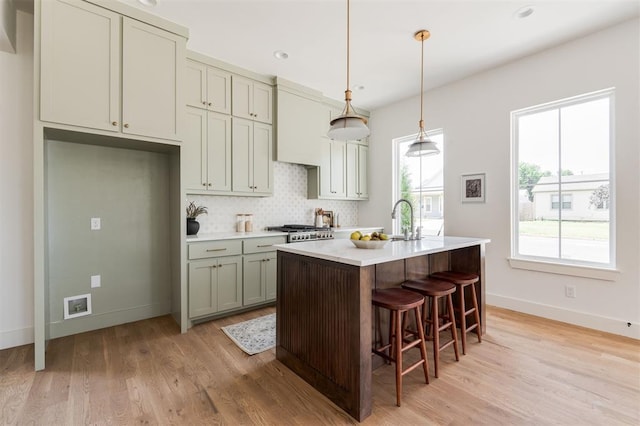 kitchen with pendant lighting, backsplash, a kitchen bar, a kitchen island with sink, and light hardwood / wood-style flooring