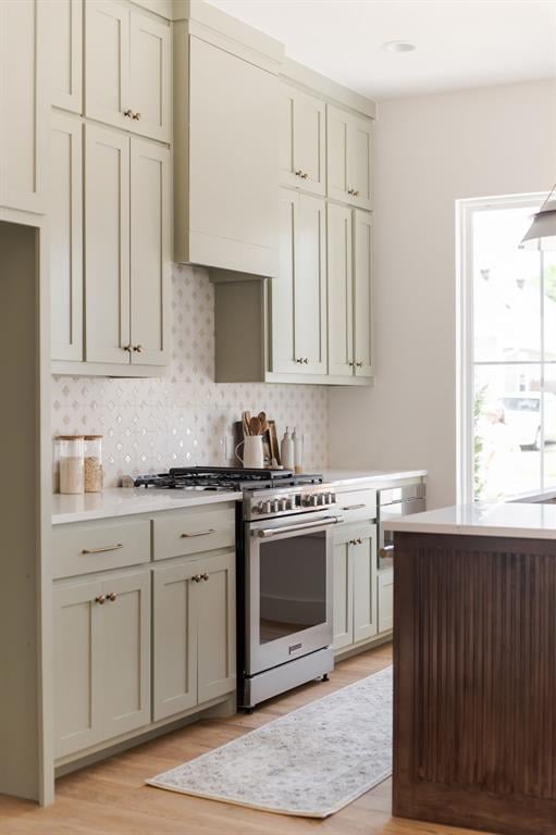 kitchen featuring high end stainless steel range oven, tasteful backsplash, custom range hood, and light hardwood / wood-style flooring