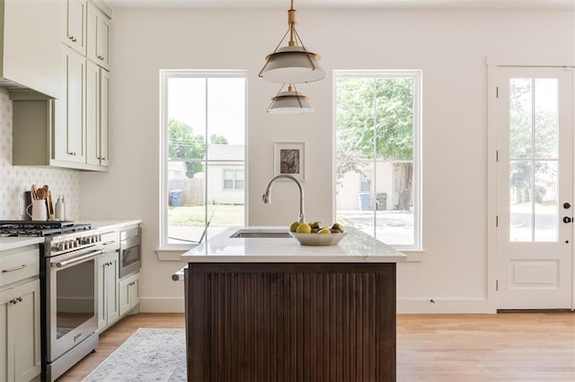 kitchen featuring high end stainless steel range oven, a wealth of natural light, hanging light fixtures, and a center island with sink