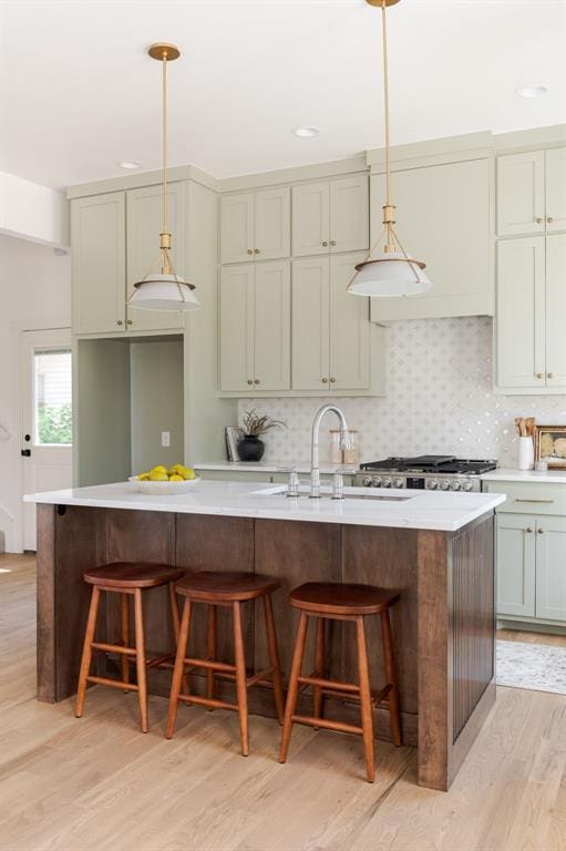 kitchen featuring sink, a breakfast bar area, hanging light fixtures, an island with sink, and decorative backsplash