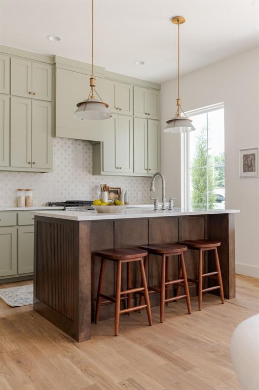 kitchen with pendant lighting, backsplash, light hardwood / wood-style flooring, and a kitchen bar