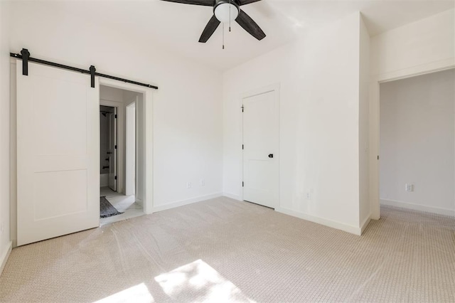 unfurnished bedroom with a barn door, light carpet, and ceiling fan