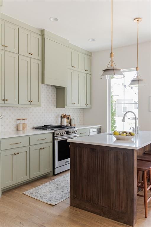 kitchen featuring decorative light fixtures, a center island with sink, stainless steel stove, light hardwood / wood-style floors, and backsplash