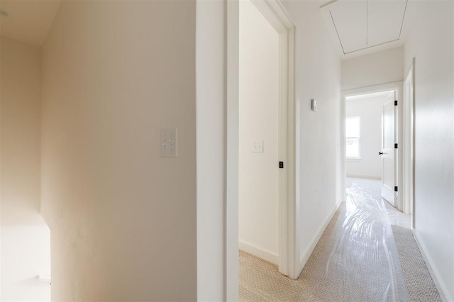 hallway with attic access, light colored carpet, and baseboards