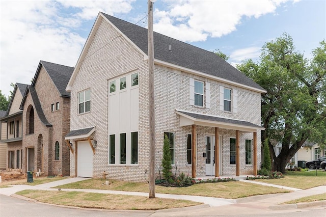 multi unit property with a garage, brick siding, a front yard, and a shingled roof