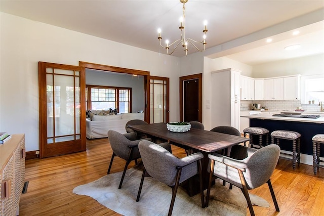 dining space featuring french doors, light wood-type flooring, and a notable chandelier