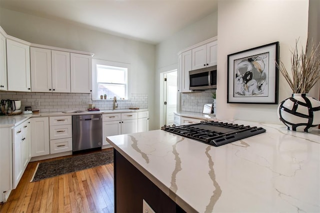 kitchen featuring sink, light stone counters, stainless steel appliances, white cabinets, and decorative backsplash