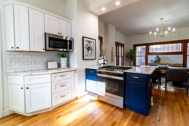 kitchen with blue cabinetry, appliances with stainless steel finishes, white cabinets, and pendant lighting