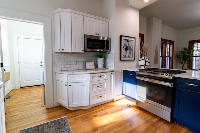 kitchen with blue cabinetry, appliances with stainless steel finishes, white cabinetry, and light wood-type flooring