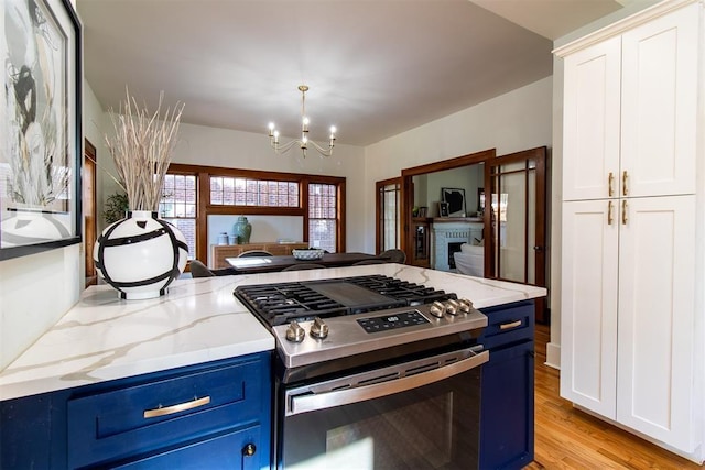 kitchen with stainless steel gas range oven, blue cabinetry, light stone countertops, white cabinets, and decorative light fixtures