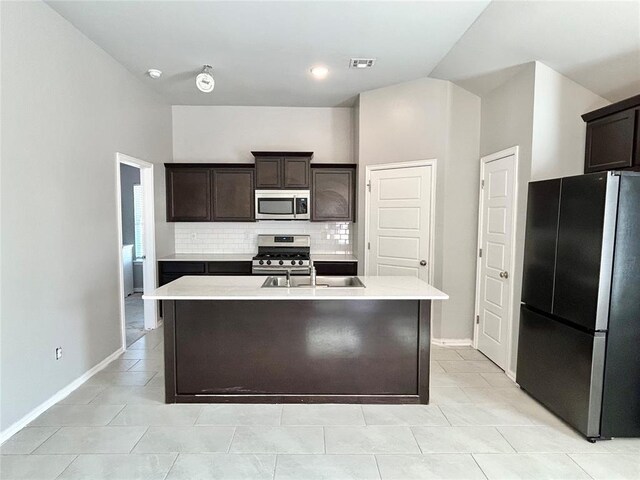 kitchen with decorative backsplash, appliances with stainless steel finishes, dark brown cabinetry, and an island with sink