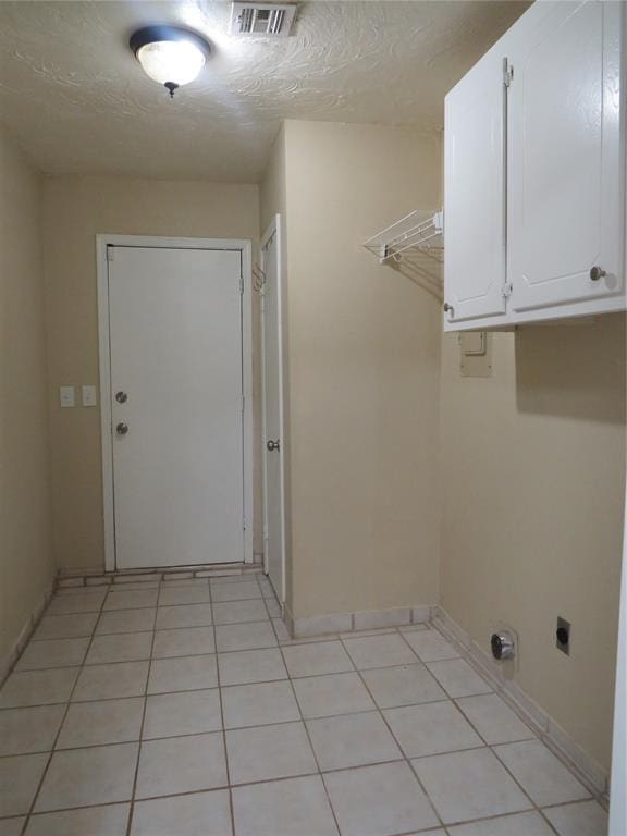 washroom with electric dryer hookup, light tile patterned flooring, and cabinets