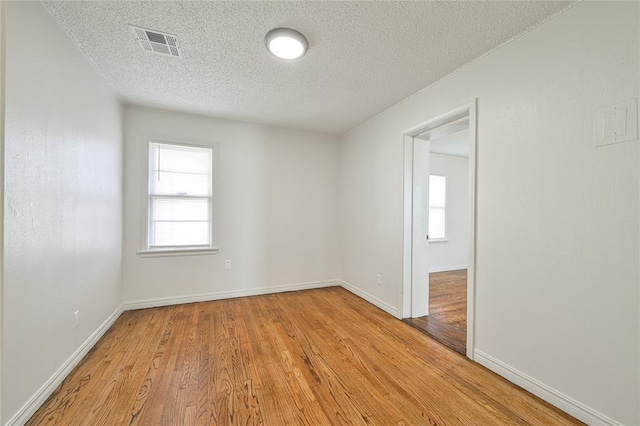 empty room with plenty of natural light, light hardwood / wood-style floors, and a textured ceiling