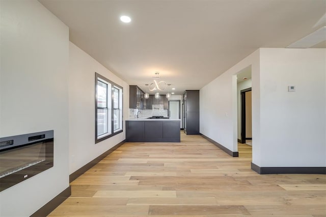 kitchen with kitchen peninsula, light wood-type flooring, backsplash, and a chandelier