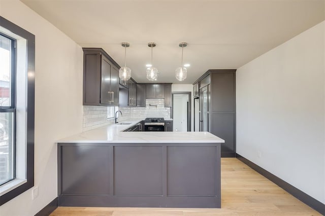 kitchen featuring tasteful backsplash, kitchen peninsula, sink, and decorative light fixtures