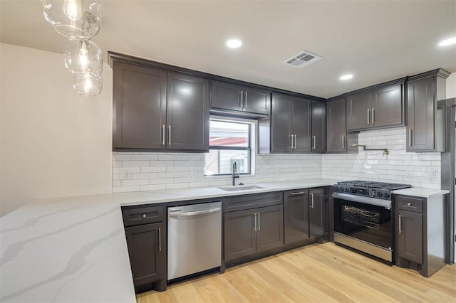 kitchen featuring light stone countertops, sink, hanging light fixtures, light hardwood / wood-style flooring, and appliances with stainless steel finishes