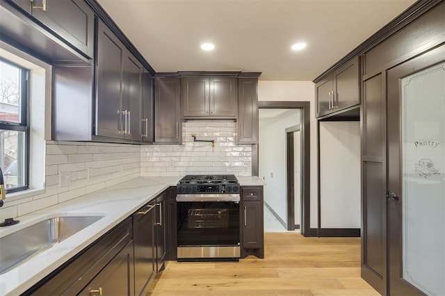 kitchen featuring light stone counters, dark brown cabinets, sink, stainless steel gas stove, and light hardwood / wood-style floors