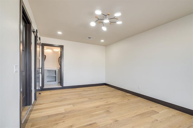 unfurnished room featuring a notable chandelier, a barn door, and light wood-type flooring