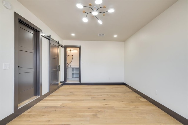 unfurnished room featuring a barn door, an inviting chandelier, and light wood-type flooring