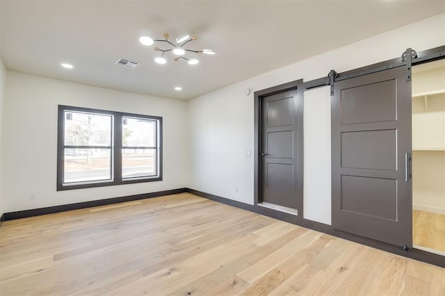 unfurnished bedroom featuring a barn door, light hardwood / wood-style floors, and an inviting chandelier