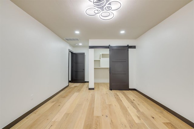 unfurnished bedroom featuring a barn door, light hardwood / wood-style floors, and a closet