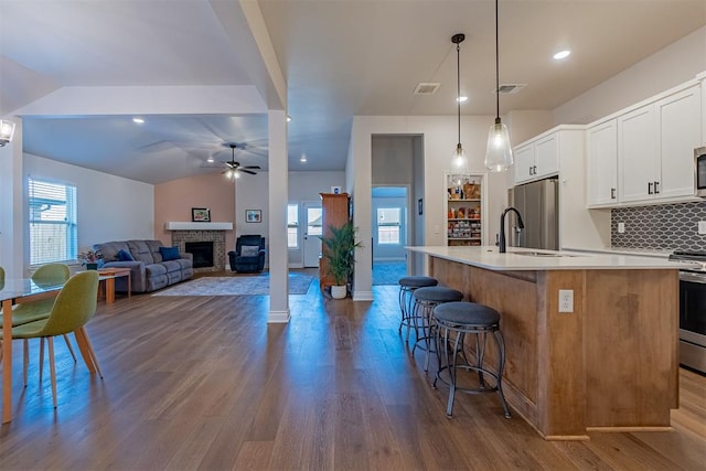 kitchen with backsplash, white cabinets, a center island with sink, ceiling fan, and decorative light fixtures