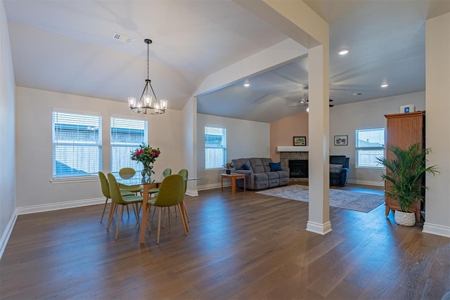 dining room with ceiling fan with notable chandelier, vaulted ceiling, dark hardwood / wood-style floors, and a brick fireplace