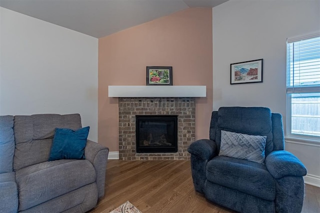 living room featuring a brick fireplace, a healthy amount of sunlight, hardwood / wood-style floors, and vaulted ceiling