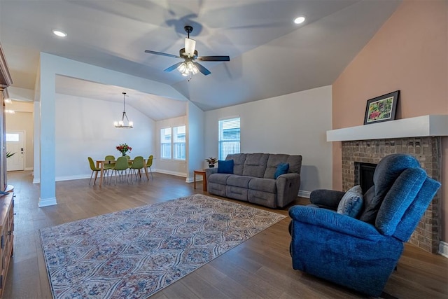 living room featuring a fireplace, hardwood / wood-style floors, ceiling fan with notable chandelier, and vaulted ceiling