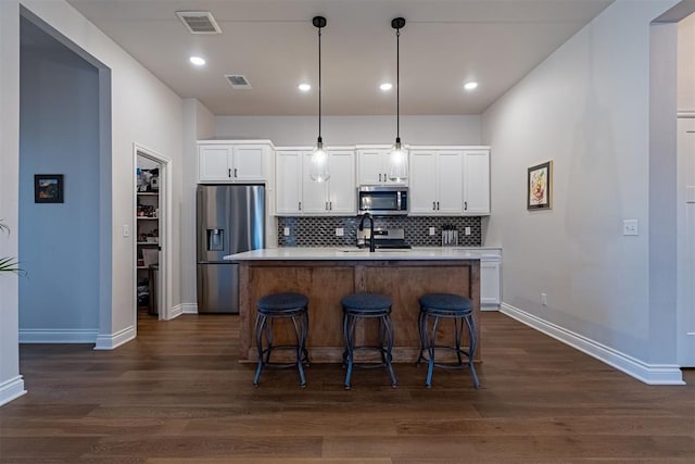 kitchen featuring a kitchen island with sink, hanging light fixtures, white cabinets, and stainless steel appliances