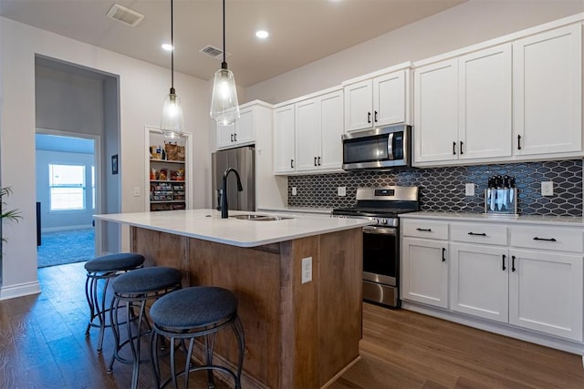 kitchen featuring a center island with sink, decorative light fixtures, white cabinets, and stainless steel appliances