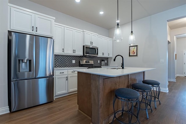 kitchen featuring backsplash, an island with sink, appliances with stainless steel finishes, decorative light fixtures, and white cabinetry