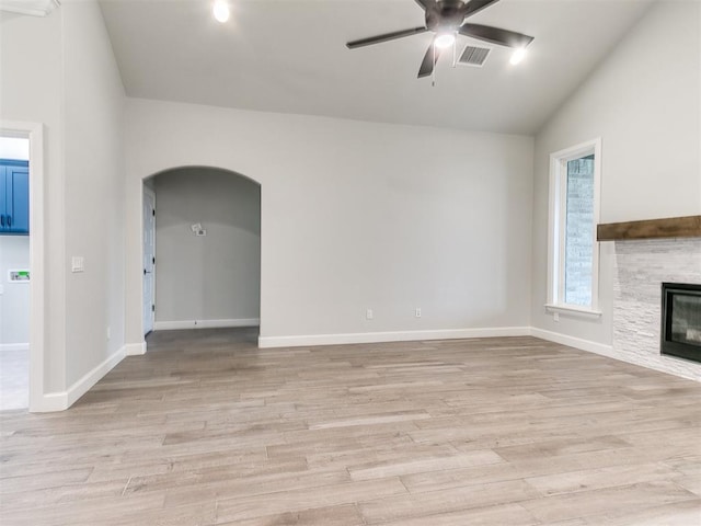 unfurnished living room featuring light hardwood / wood-style flooring, a stone fireplace, ceiling fan, and lofted ceiling