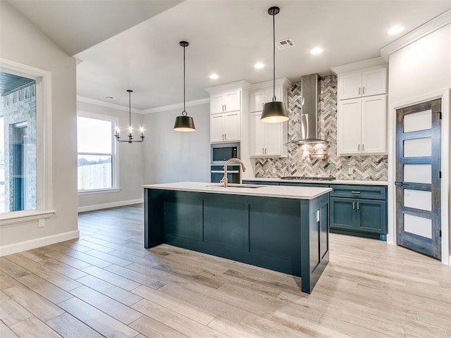 kitchen with built in microwave, white cabinetry, wall chimney exhaust hood, decorative light fixtures, and a center island with sink