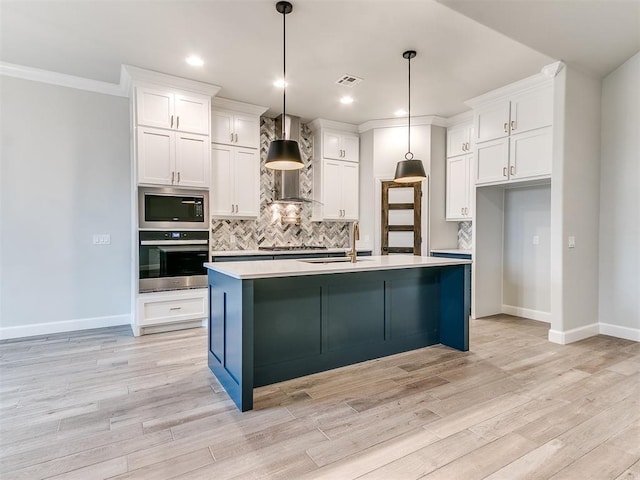 kitchen with white cabinets, pendant lighting, stainless steel appliances, and wall chimney exhaust hood