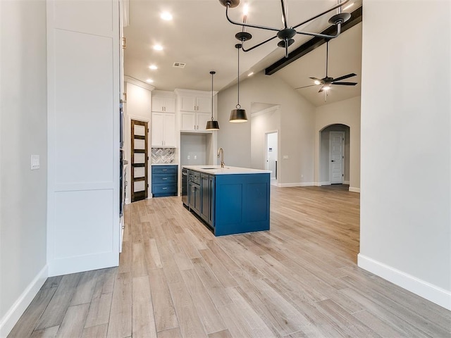 kitchen with blue cabinetry, white cabinetry, a kitchen island with sink, light hardwood / wood-style floors, and decorative backsplash