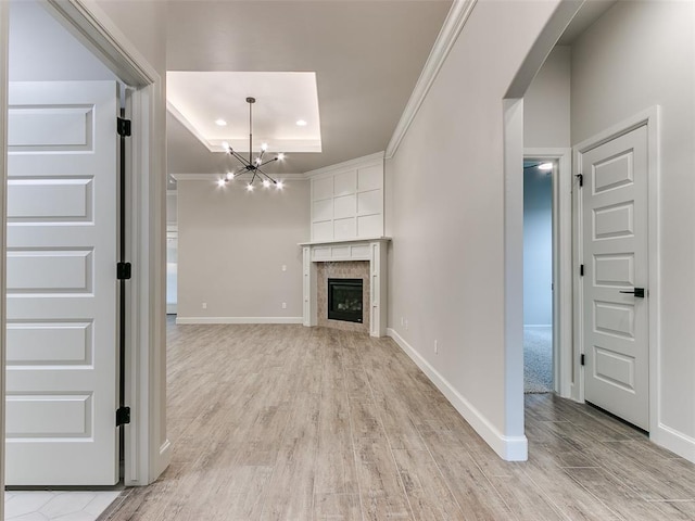 unfurnished living room featuring a notable chandelier, a raised ceiling, light wood-type flooring, and ornamental molding